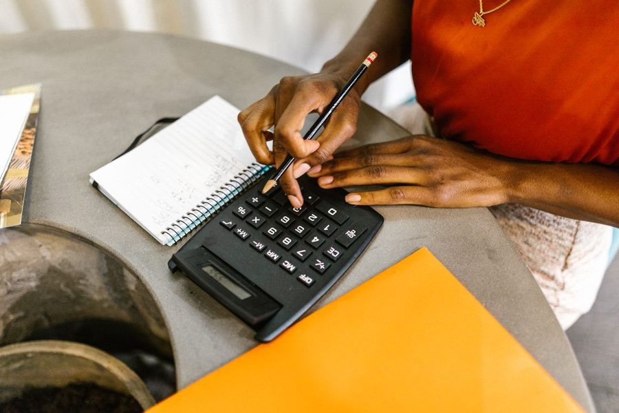 A Black woman reviewing numbers with a calculator and notebook.