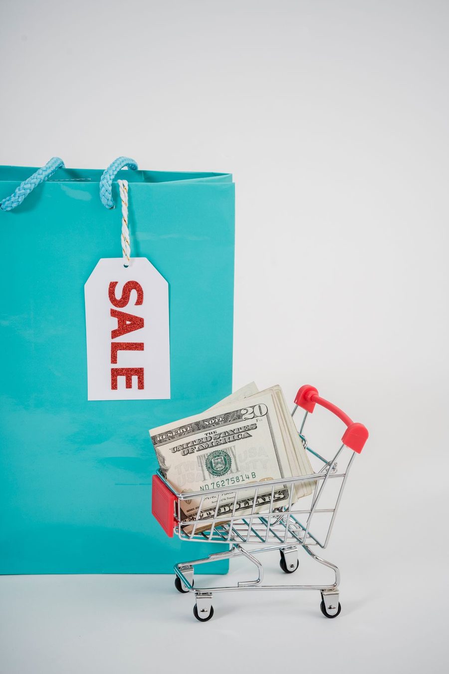A miniature shopping cart, cash and a sale bag representing coupon savings.