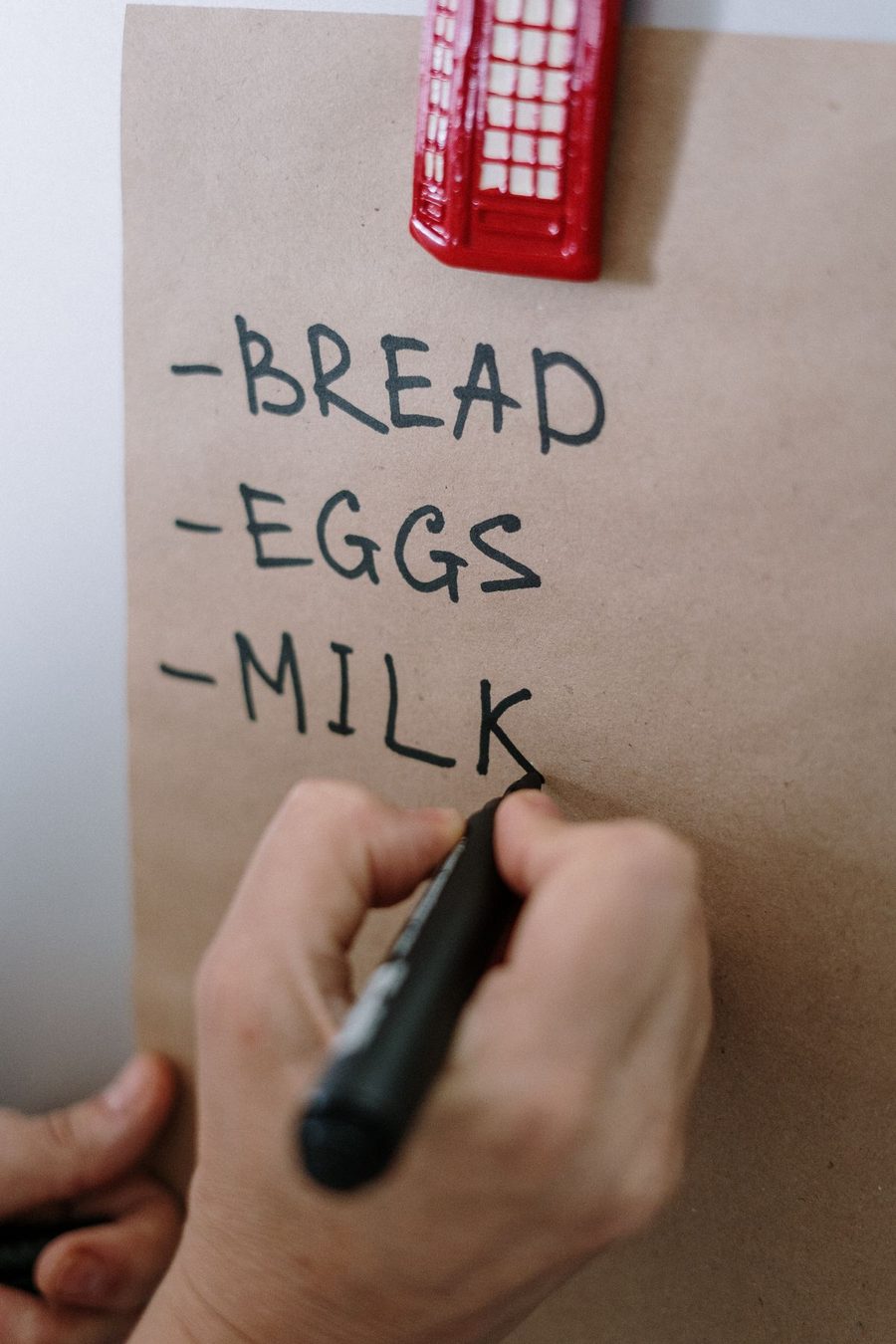 A hand writing a short grocery list for everyday staples.