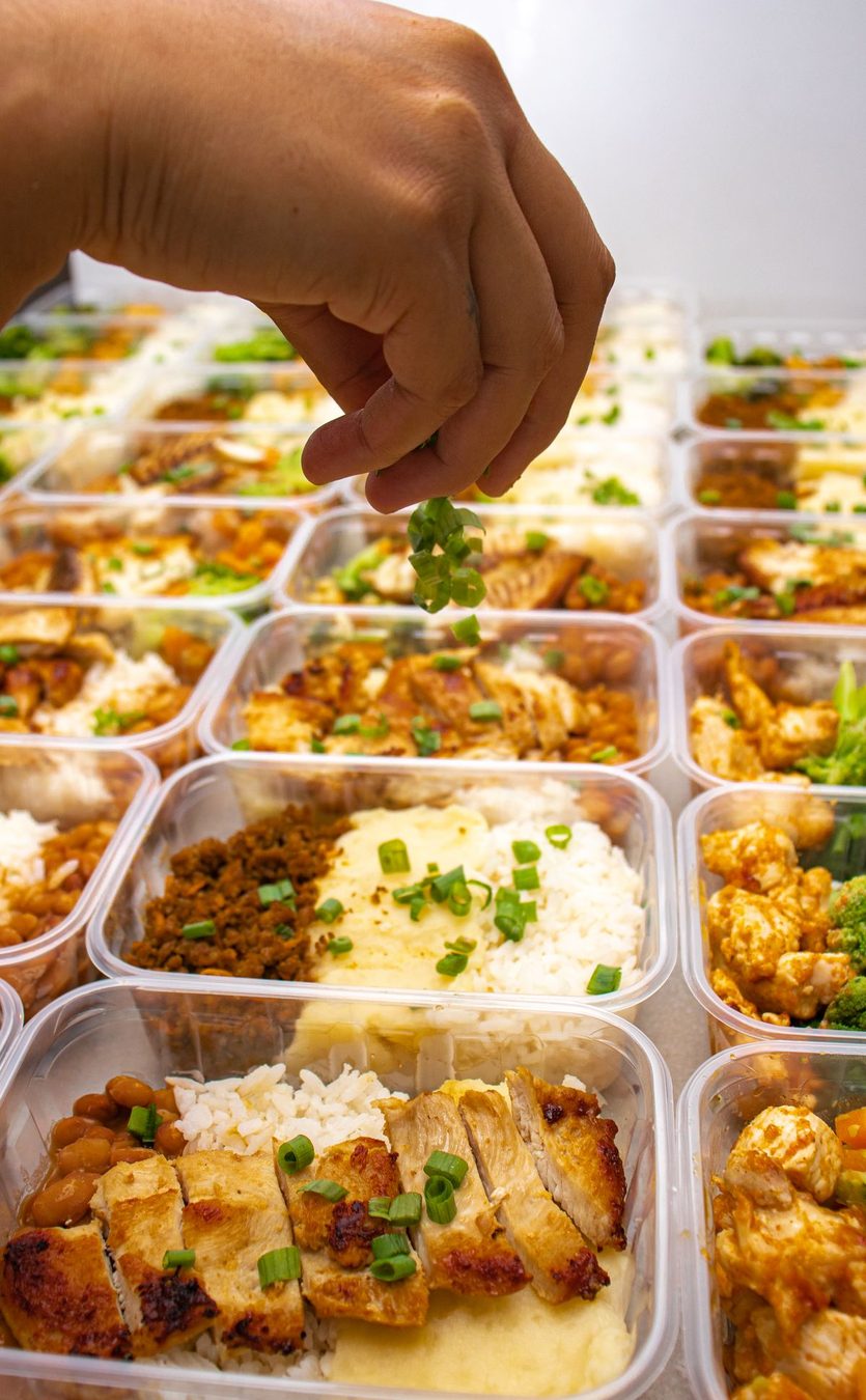 Hands preparing a meal in fresh containers for the week.