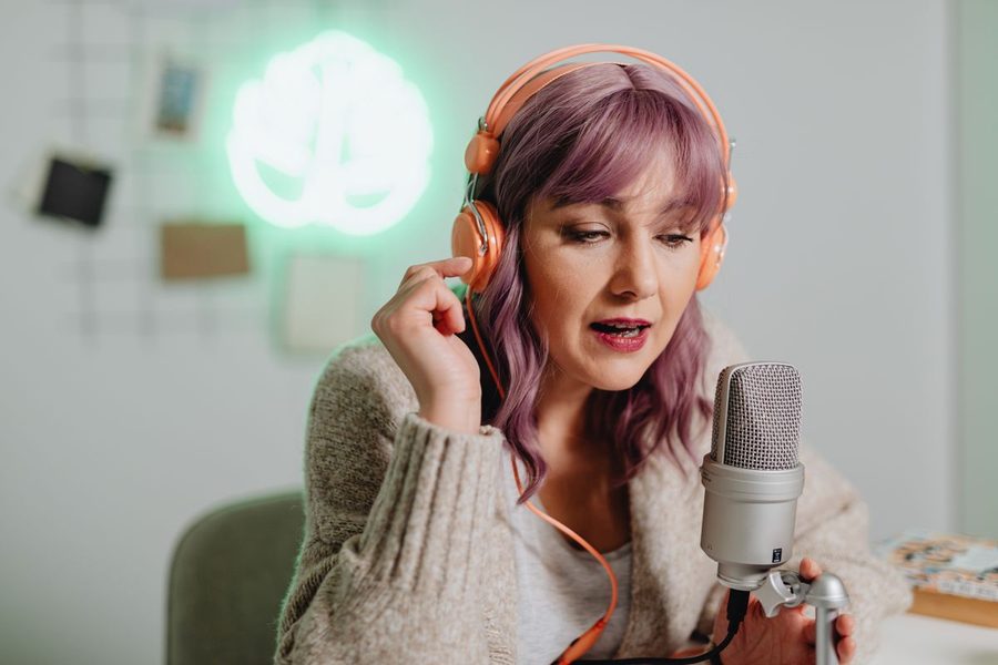 A woman recording a podcast at home with headphones and a microphone.