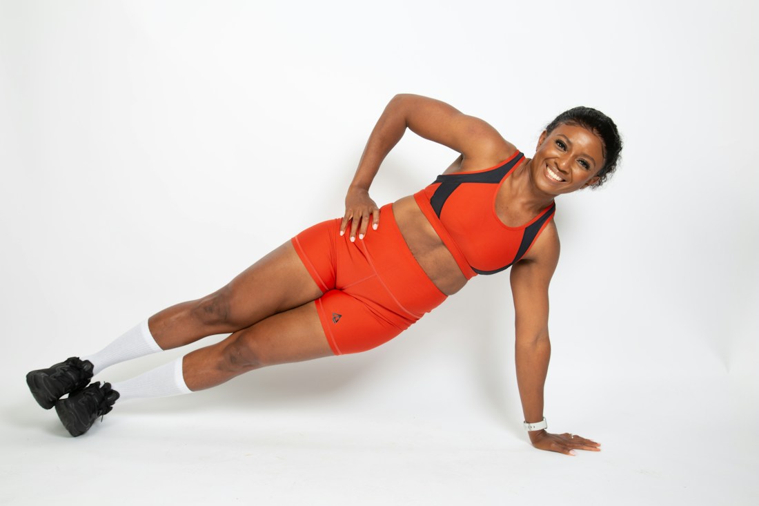 Black woman in orange fitness wear holding a plank with abs visible